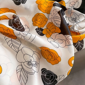 Détail de l'imprimé camélia sur une écharpe soyeuse aux tons élégants d'orange et de noir
