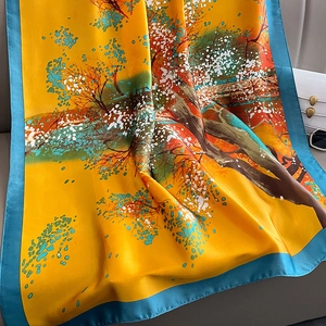 Elegant mustard silk scarf with landscape print and teal borders draped on a sofa