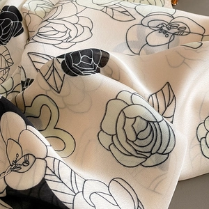 Détail d'un foulard en soie montrant un motif de camélia et une texture de tissu fluide