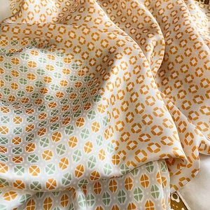 Close-up of elegant silk scarf featuring geometric orange and green patterns on ivory fabric