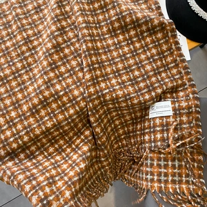 Gros plan sur un châle à carreaux d'hiver avec pompons orange et étiquette tissée chic