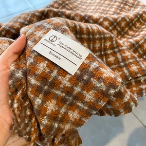 Gros plan d'une écharpe en tricot à carreaux avec fils dorés et étiquette tissée