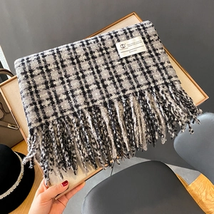Détail d'une écharpe à carreaux gris avec pompons doux et étiquette carrée tissée