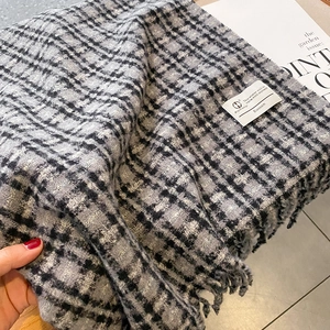 Détail d'une écharpe en cachemire à carreaux noir et gris avec franges et fils métallisés