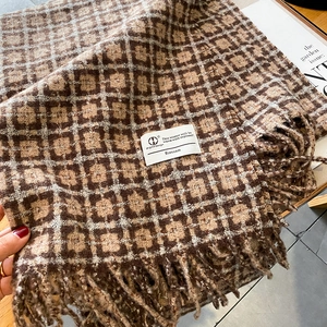Détail d'une écharpe épaisse à carreaux marron avec des franges douces et étiquette blanche