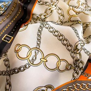 Macro shot of luxury silk-like scarf featuring golden chain and belt buckle patterns