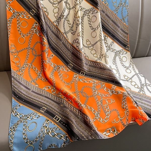 Elegant silk-like scarf with orange and blue chain print pattern on dark leather background