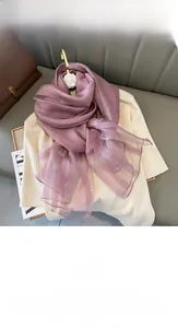 Detail of silk blend scarf in mauve pink draped over a beige knit top on a sofa