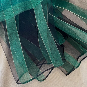 Detail of silk blend scarf fabric with green and black pleated layers and gold metallic stripes