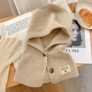 Détail de la cagoule en maille beige avec boutons texturés et étiquette de marque tissée