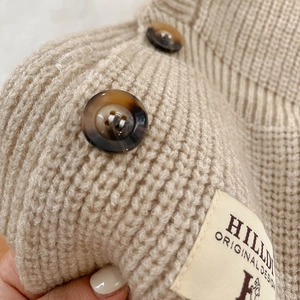Détail de maille épaisse avec boutons en écaille et étiquette de marque sur tissu beige