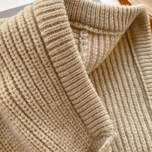Gros plan sur la maille épaisse côtelée et les détails doux du col de ce bonnet beige