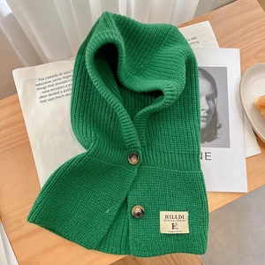 Détail de la cagoule en tricot vert avec boutons foncés et étiquette sur bois