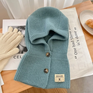 Détail d'une capuche en grosse maille bleu canard avec boutons et étiquette sur bois