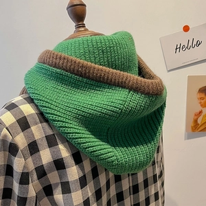 Detail eines grün-braunen handgestrickten Kapuzenschals mit Ohrenklappen auf einer Holzpuppe