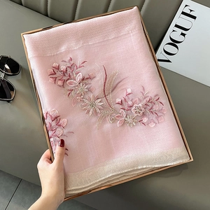 Detail of pink silk scarf with floral embroidery and golden glitter hem on a tray