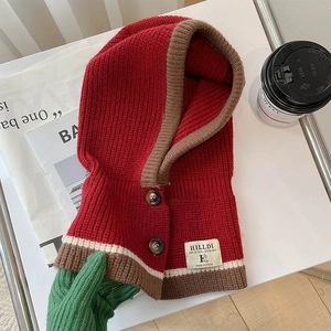 Detail eines roten Strickschal-Kapuze mit Knöpfen und Markenetikett auf gemütlichem Tisch