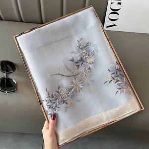 Close-up of elegant floral embroidery on a sheer blue silk blend shawl in a metal frame