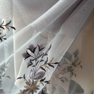 Close-up of floral embroidery on elegant silk blend fabric with golden and purple threads