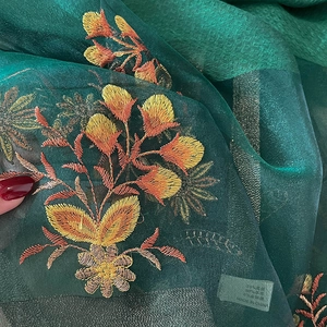 Macro detail of embroidered floral patterns on dark green semi-transparent silk blend fabric