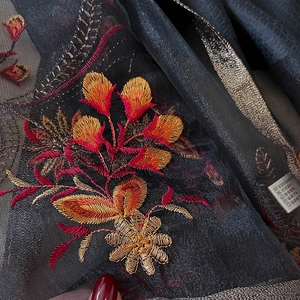 Macro detail of floral embroidery on black silk blend scarf with golden metallic edges