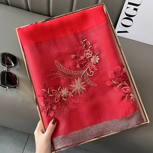 Detail of red silk blend shawl with floral embroidery folded in a gold metal tray