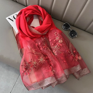 Detail of red silk blend scarf with intricate gold embroidery on a luxury leather bench