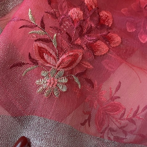 Detail of red silk blend fabric with intricate gold floral embroidery and woven hem