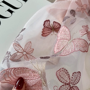Détail macro d'une broderie papillon rose sur la texture d'une écharpe en soie
