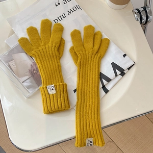 Detail of ginger yellow knitted gloves featuring a thick ribbed texture and woven label tag