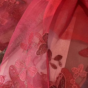 Détail macro d'une écharpe en soie et laine rouge avec broderie florale et fils métalliques