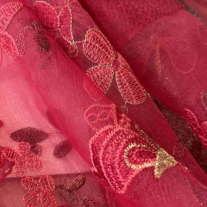 Gros plan du tissu élégant en laine de soie bordeaux avec broderie florale et fil doré