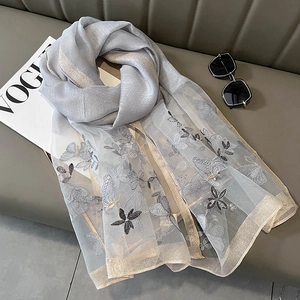 Détail de l'écharpe en soie grise avec broderie papillon sur un canapé en cuir gris