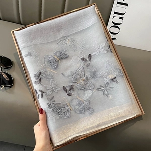 Détail de broderie papillon 3D sur un châle gris en soie et laine dans son coffret
