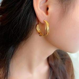 Detailed view of irregular twisted gold hoop earring with frosted texture on ear