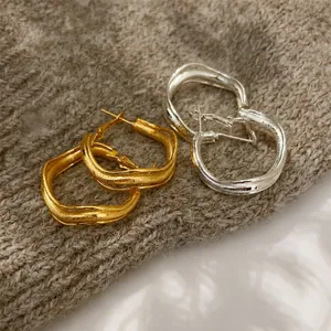 Macro detail of gold and silver twisted hoop earrings on soft knit texture