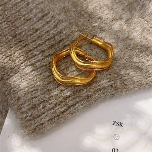 Detail of gold twisted hoop earrings with frosted finish on grey knit background