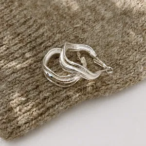 Macro shot of silver wave earrings with a liquid metal texture and polished finish