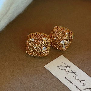 Golden hollow cube earrings with white zircon accents on a textured background