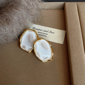 Irregular oval gold-plated resin earrings with mother of pearl finish on brown velvet tray