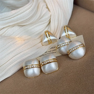 Macro detail of geometric stud earrings with matte pearl finish and zircon inlays