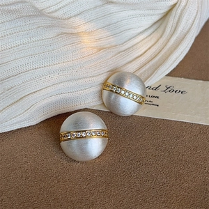 Detailed view of matte silver stud earrings with a gold band and inlaid crystals