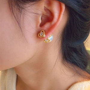 Detail of heart-shaped gold earring with zircon and pearl on model's ear