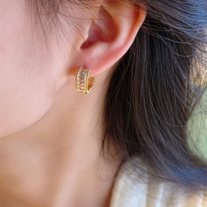 Golden C-shaped earrings with square zircons worn by a model in a close-up shot