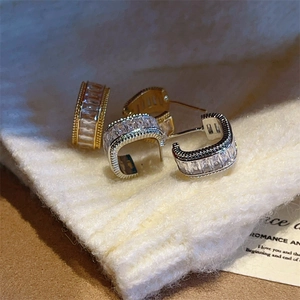 Detail of gold and silver C-shaped hoop earrings with zircon on a knit sweater
