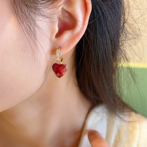 Close-up of heart-shaped red zircon earrings with gold finish worn by a model