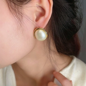 Elegant gold-edged round faux pearl stud earrings worn by a model for a vintage look