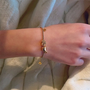 Detail of hand wearing gold coin bracelet with braided black rope and sparkling rhinestones