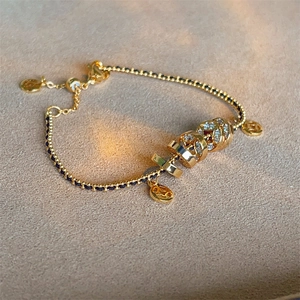 Close-up of adjustable black braided bracelet with gold beads and H-logo charm