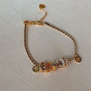 Braided black rope bracelet with gold coins and zircon beads on beige fabric